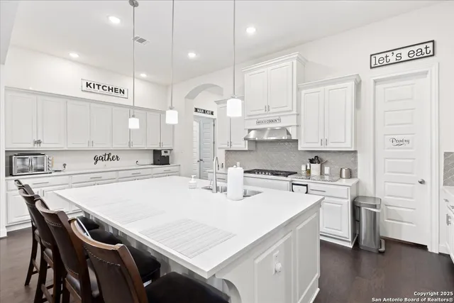 a kitchen with stainless steel appliances granite countertop a sink a stove a refrigerator and white cabinets with wooden floor