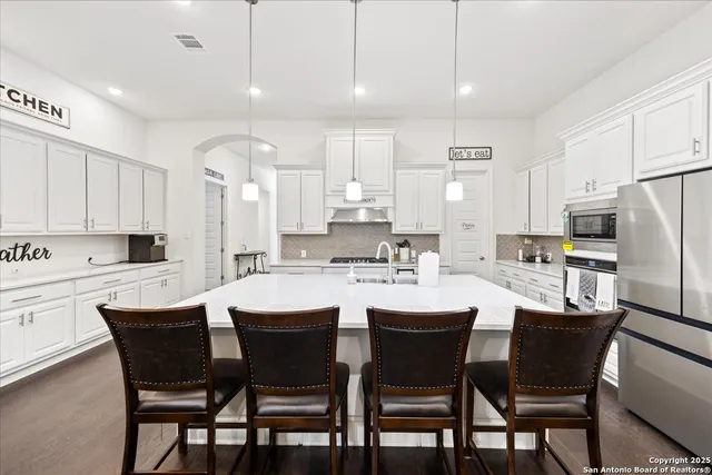 a kitchen with a dining table chairs wooden floor cabinets and appliances