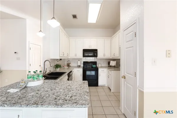 a kitchen with stainless steel appliances granite countertop a refrigerator a stove a sink and white cabinets with wooden floor