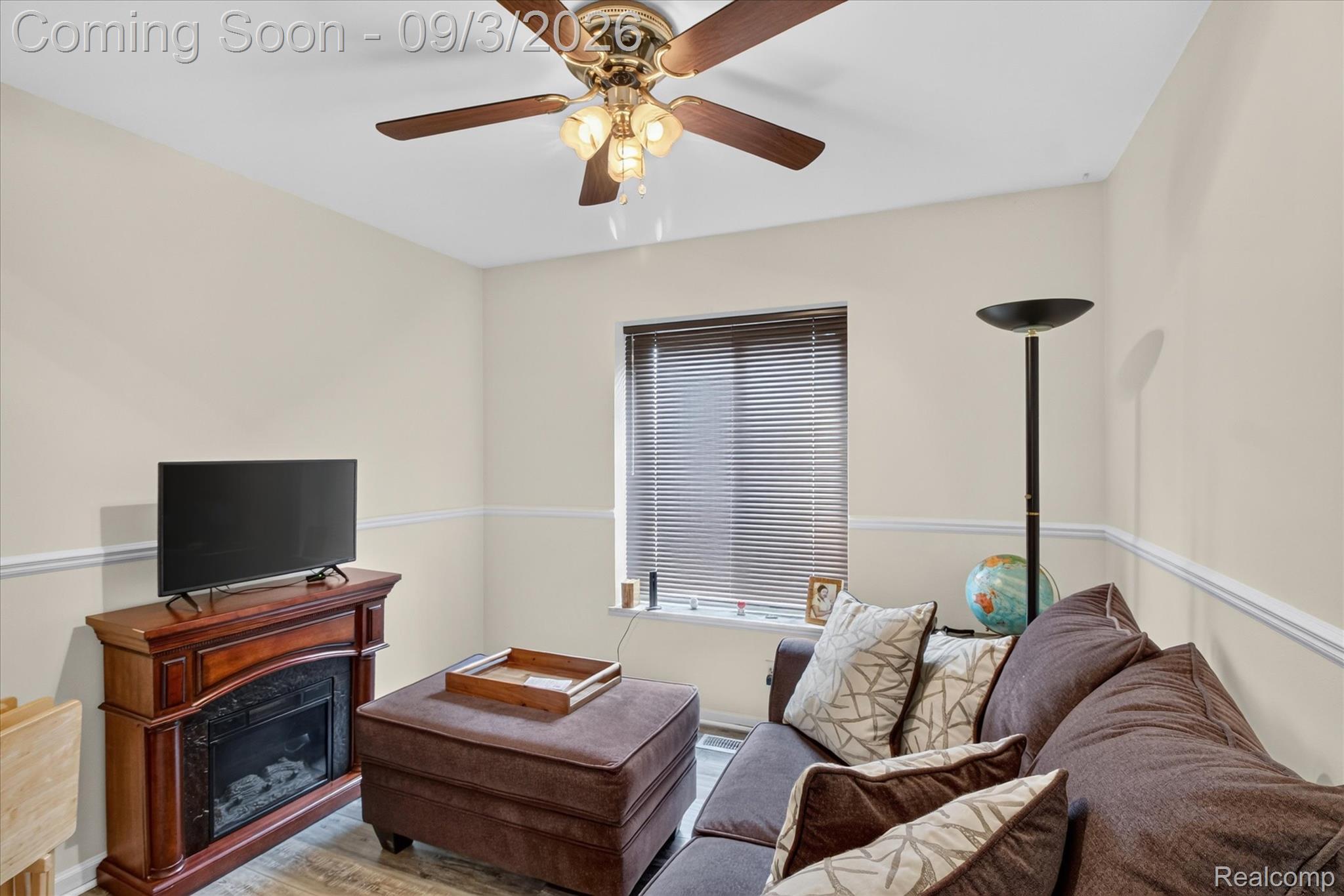 27260 Campbell Road Warren, MI 48093 - Photo 27 of 60 Recessed window with blinds, wood-finish flooring, ceiling fan with integrated lighting, chair rail molding, and an electric fireplace with a wood-finish mantel