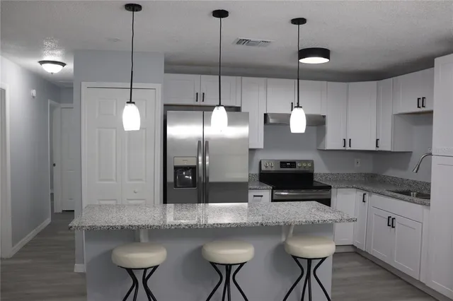 a kitchen with stainless steel appliances granite countertop a sink a stove a refrigerator and white cabinets with wooden floor