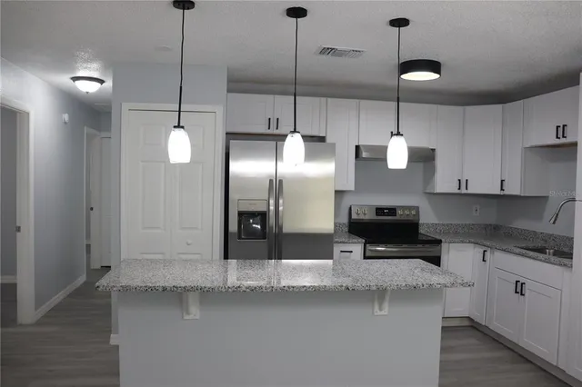 a kitchen with stainless steel appliances granite countertop a sink a refrigerator a stove and white cabinets with wooden floor