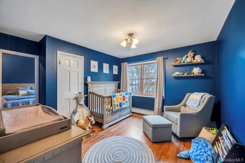 39 Bevin Road Northport, NY 11768 - Photo 24 of 44 Bedroom featuring wood finished floors, a baseboard heating unit, a crib, and a closet