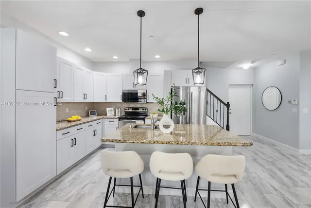 a kitchen with stainless steel appliances kitchen island granite countertop a dining table chairs and white cabinets