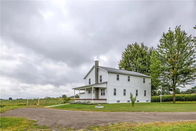 a view of a white house next to a yard with big trees
