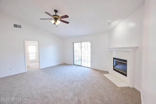 a view of an empty room with chandelier fan and fire place