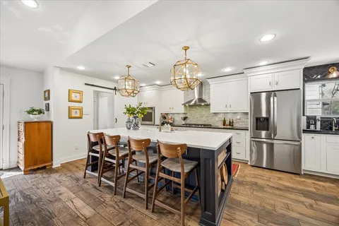 a kitchen with stainless steel appliances kitchen island granite countertop a refrigerator a stove a microwave oven a dining table and chairs with wooden floor
