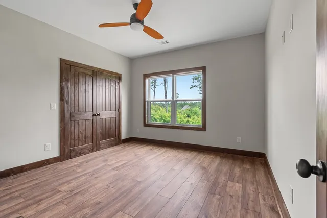 an empty room with wooden floor chandelier fan and windows