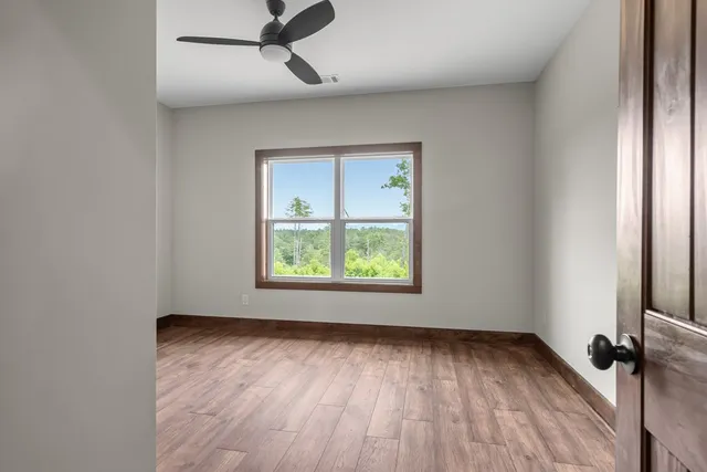 an empty room with wooden floor fan and windows