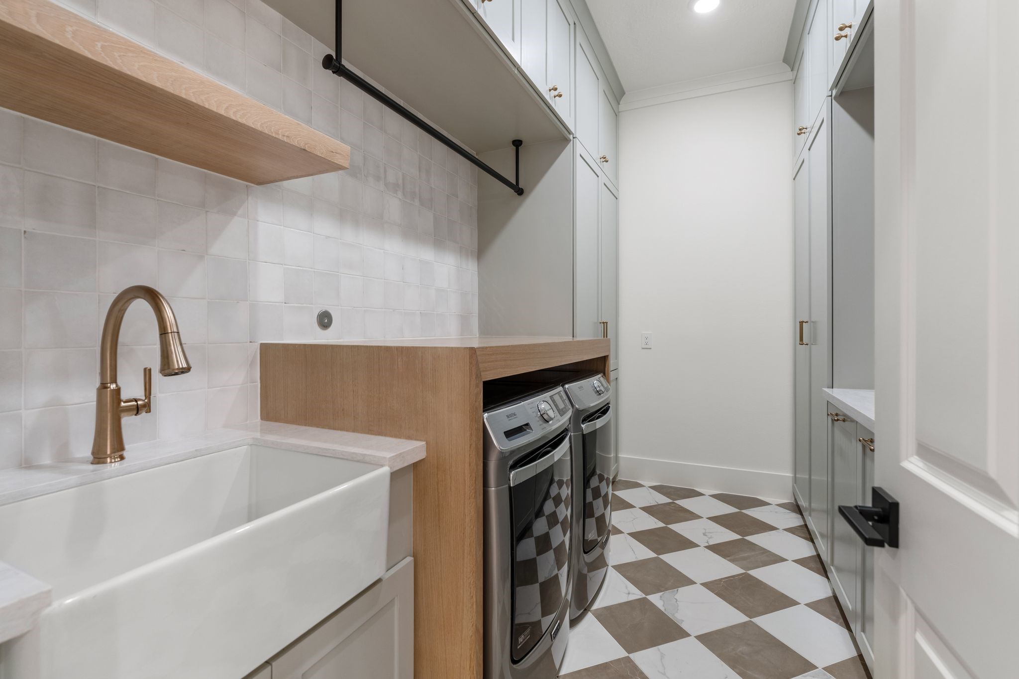 31 Hollymead Drive Spring, TX 77381 - Photo 17 of 50 This is a modern laundry room featuring a farmhouse sink, sleek cabinetry, and 2026 washer-dryer set. The space has a stylish checkered tile flooring and ample storage, offering functionality and elegance.