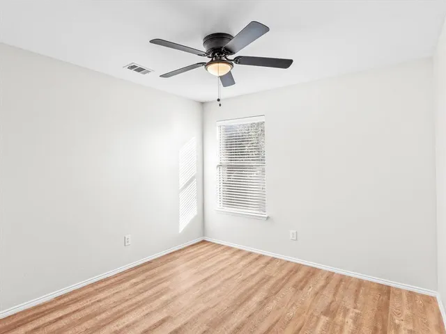 an empty room with wooden floor ceiling fan and windows