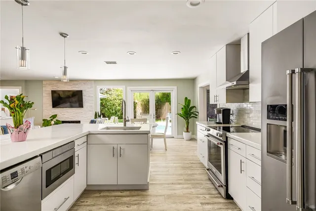 a kitchen with stainless steel appliances a stove top oven a sink dishwasher a refrigerator white cabinets and wooden floor