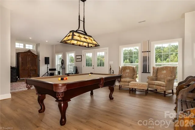 a room with lots of furniture pool table wooden floor and windows