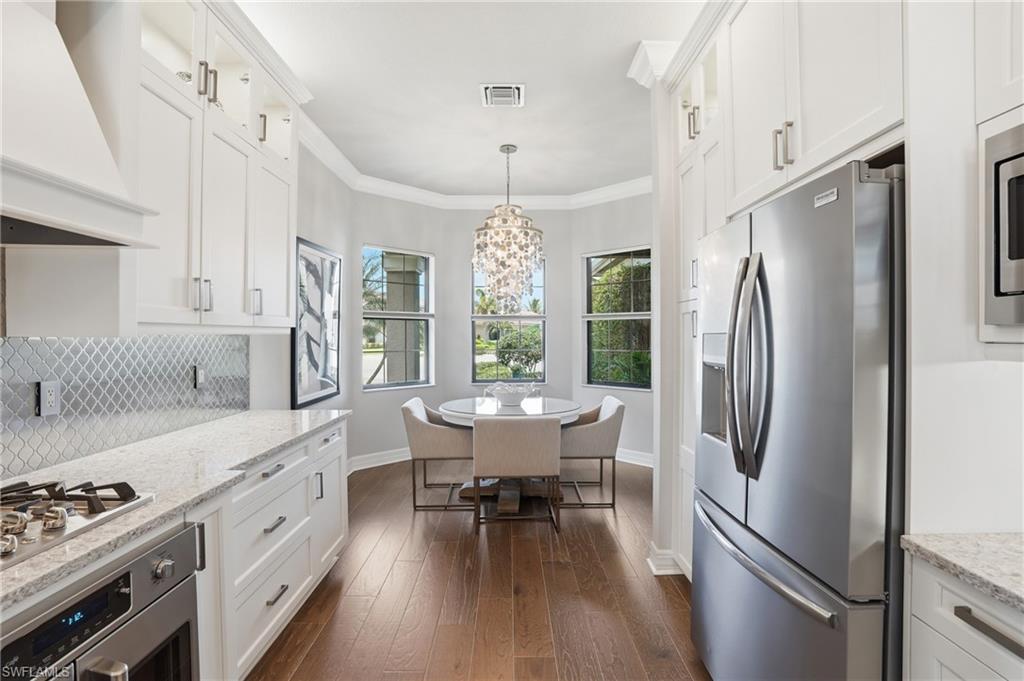 4220 Amelia Way Naples, FL 34119 - Photo 12 of 50 a kitchen with stainless steel appliances granite countertop a refrigerator a sink dishwasher a dining table and chairs with wooden floor