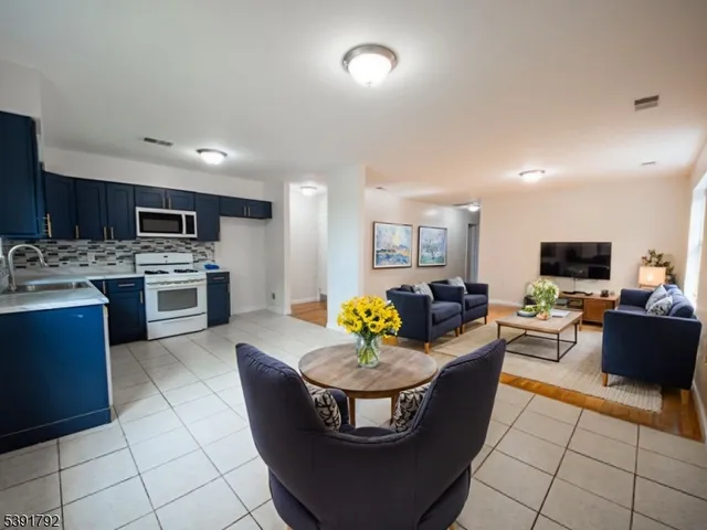 a living room with stainless steel appliances furniture a flat screen tv and kitchen view