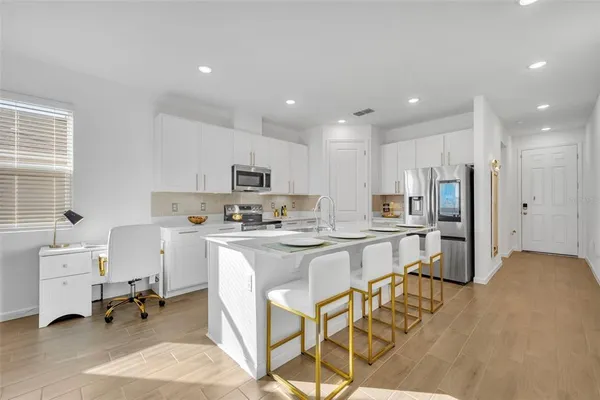 a kitchen with stainless steel appliances a stove a sink a refrigerator white cabinets and chairs