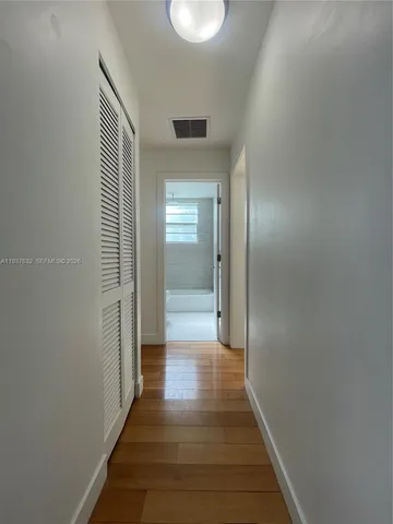 a view of a hallway with wooden floor and a bathroom