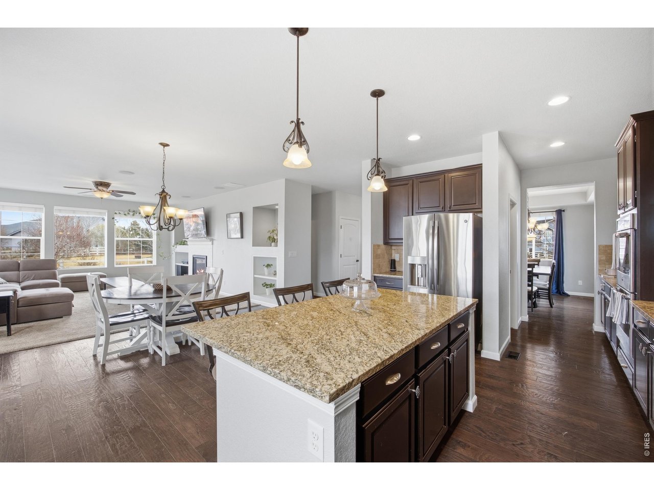 9033 Foxfire Street Firestone, CO 80504 - Photo 15 of 44 a kitchen with stainless steel appliances kitchen island granite countertop a stove a refrigerator a kitchen island a dining table and chairs with wooden floor