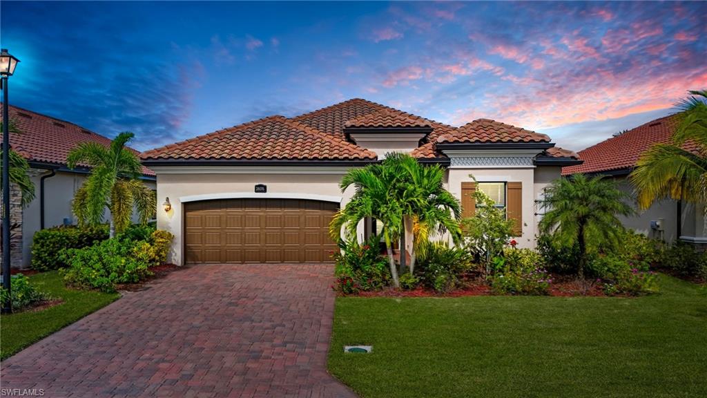 Mediterranean style home featuring stucco siding, decorative driveway, 2 car garage, tiled roof, and lush landscaping