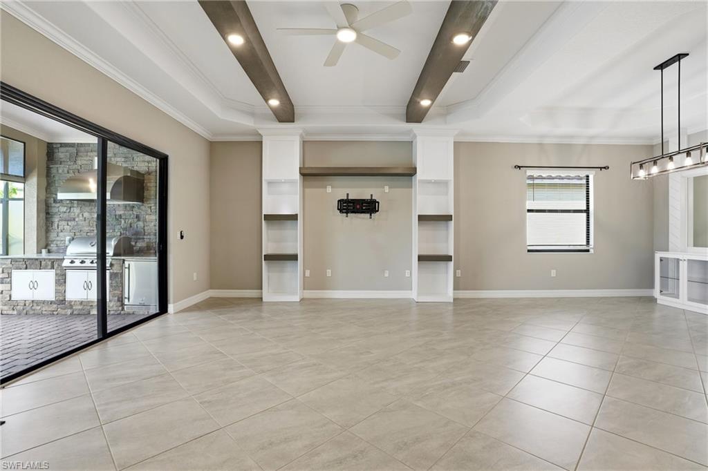 28076 Foxrock Court Bonita Springs, FL 34135 - Photo 16 of 50 Unfurnished living & dining area with custom ceiling beams, crown molding, tray ceilings, ceiling fan w/ light and controls, floor plug, custom built-in entertainment center, custom built-in buffet with ornamental molding, custom remote slider blinds (slider blinds not shown), window blinds, recessed lighting, and light tile patterned floors