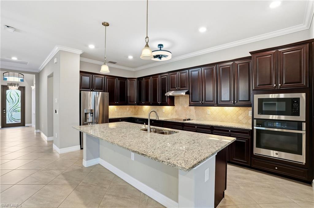 28076 Foxrock Court Bonita Springs, FL 34135 - Photo 20 of 50 Gourmet kitchen featuring crown molding, upgraded cabinets, decorative tile backsplash, pendant fixtures, granite countertops, built-in appliances, large walk in pantry with wood shelving, kitchen fan & light and tile flooring.
