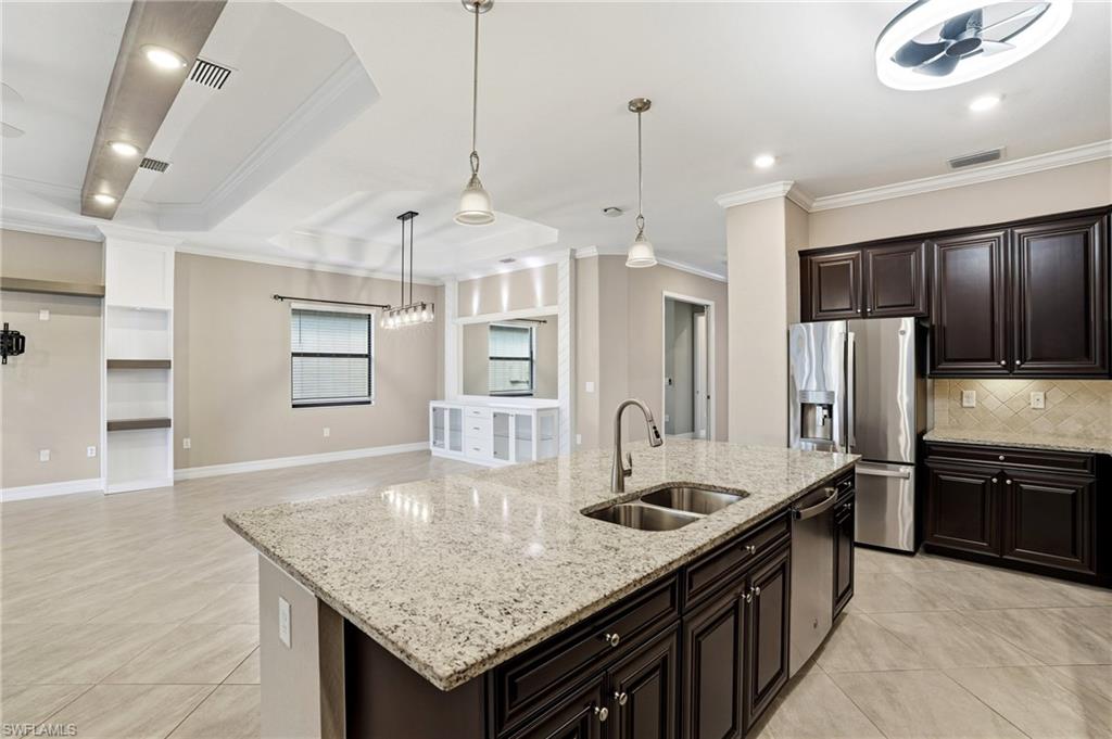 28076 Foxrock Court Bonita Springs, FL 34135 - Photo 21 of 50 Gourmet kitchen featuring crown molding, upgraded cabinets, decorative tile backsplash, pendant fixtures, granite countertops, built-in appliances, large walk in pantry with wood shelving, kitchen fan & light and tile flooring.