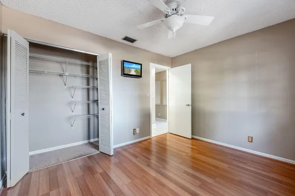 an empty room with wooden floor closet fan and windows