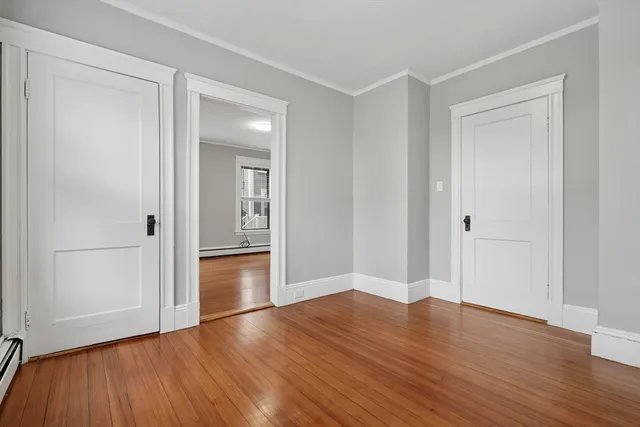 an empty room with wooden floor & cabinet and windows