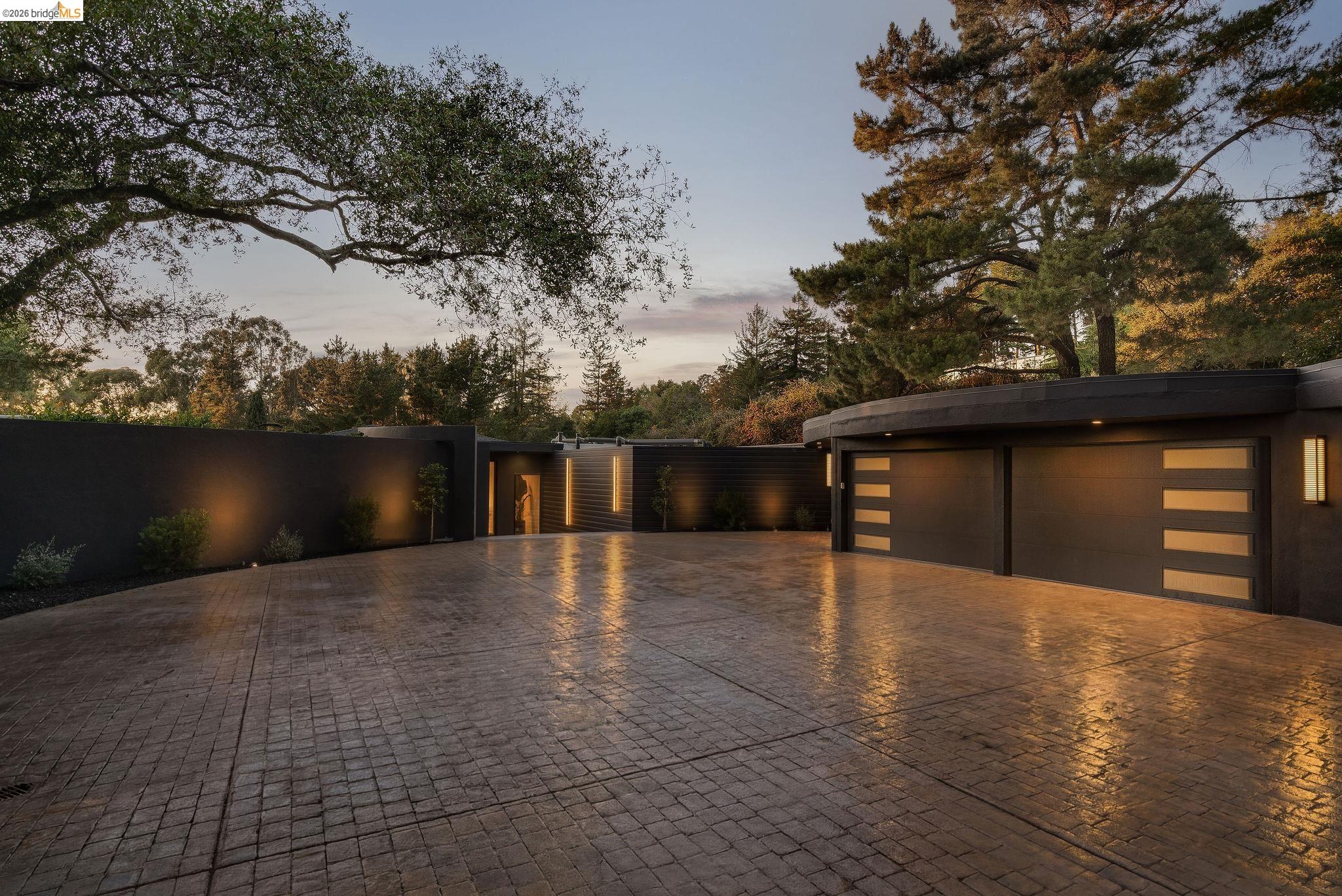 5645 Bacon Road Oakland, CA 94619 - Photo 85 of 94 Expansive stamped concrete driveway with custom exterior lighting, a curved architectural garage featuring two doors with frosted panel inserts, and a prominent solid privacy wall