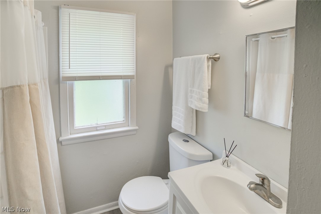 4383 Wyatt Road Cleveland, OH 44128 - Photo 14 of 33 Bathroom featuring a window with blinds, a white toilet, a vanity with an integrated sink, a wall-mounted mirror, and a brushed nickel towel bar