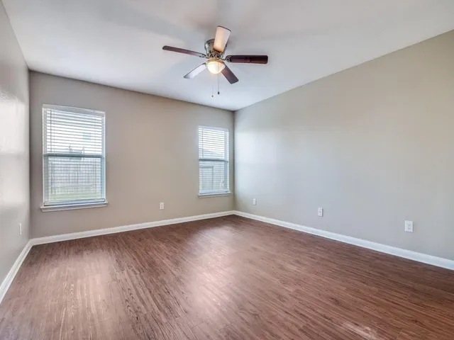 an empty room with wooden floor chandelier fan and windows