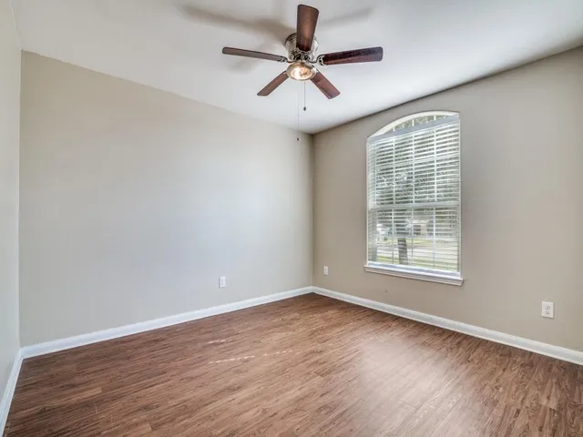 an empty room with wooden floor chandelier fan and windows