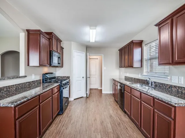 a kitchen with stainless steel appliances granite countertop wooden cabinets a stove top oven with wooden floor