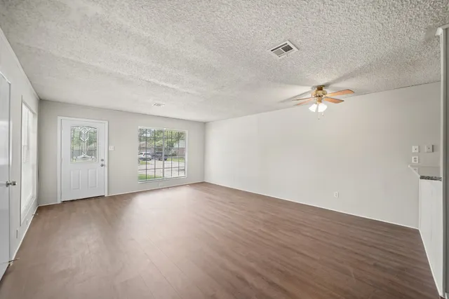 an empty room with wooden floor chandelier fan and windows
