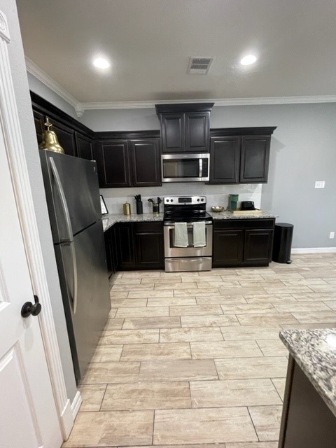 6959 Halter Loop College Station, TX 77845 - Photo 20 of 22 Kitchen featuring stainless steel appliances, dark cabinets, light stone countertops, wood tiled floors, and crown molding