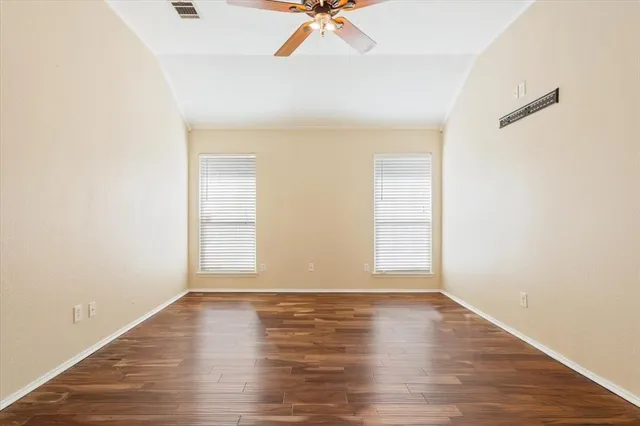 an empty room with wooden floor fan and windows