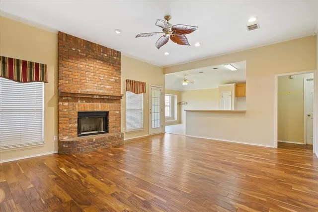 a view of a livingroom with a fireplace a ceiling fan and wooden floor