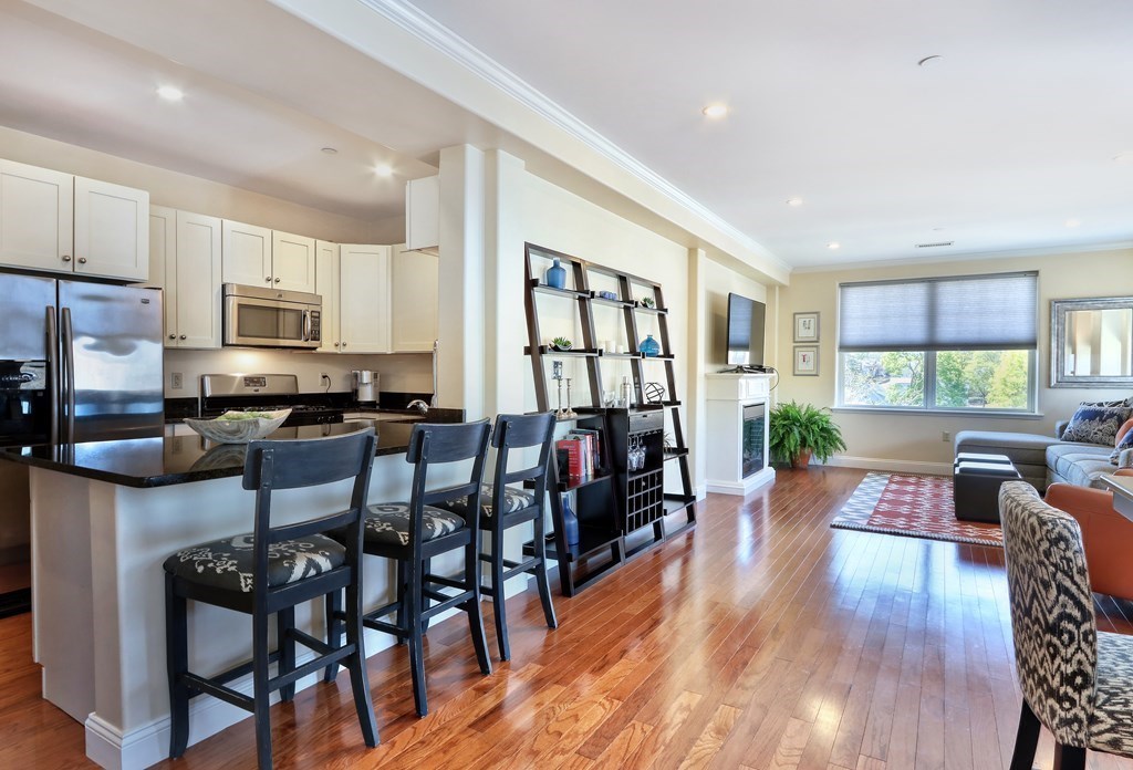 426 Main Street, Unit 402 Melrose, MA 02176 - Photo 4 of 24 a open kitchen with stainless steel appliances granite countertop a stove top oven a sink a dining table and chairs with wooden floor
