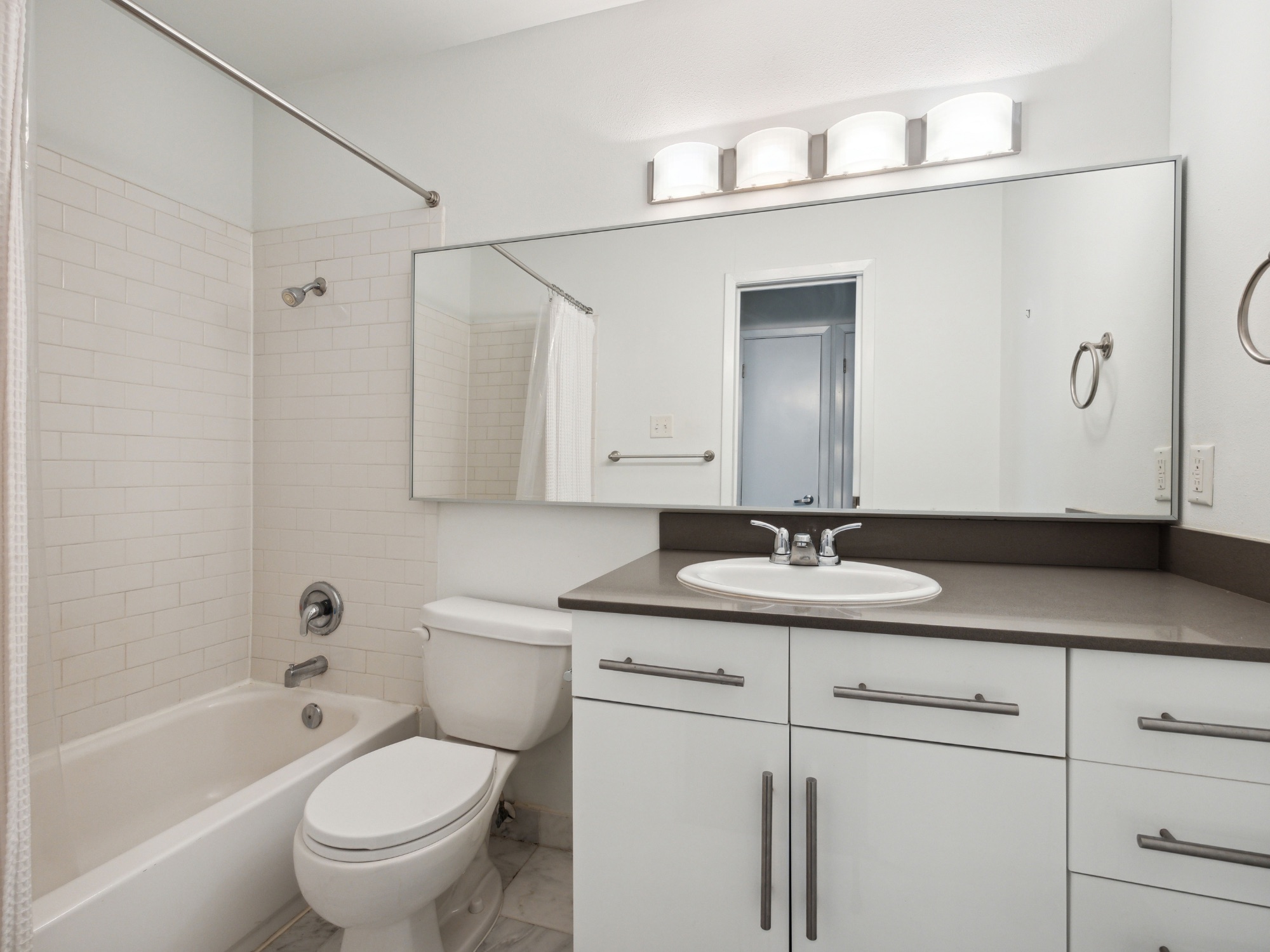 1503 West 9th Street, Unit 204 Austin, TX 78703 - Photo 14 of 21 Bathroom featuring a white subway tile shower surround, a built-in bathtub, a white vanity with multiple storage options, a grey countertop, and a large mirror with overhead lighting