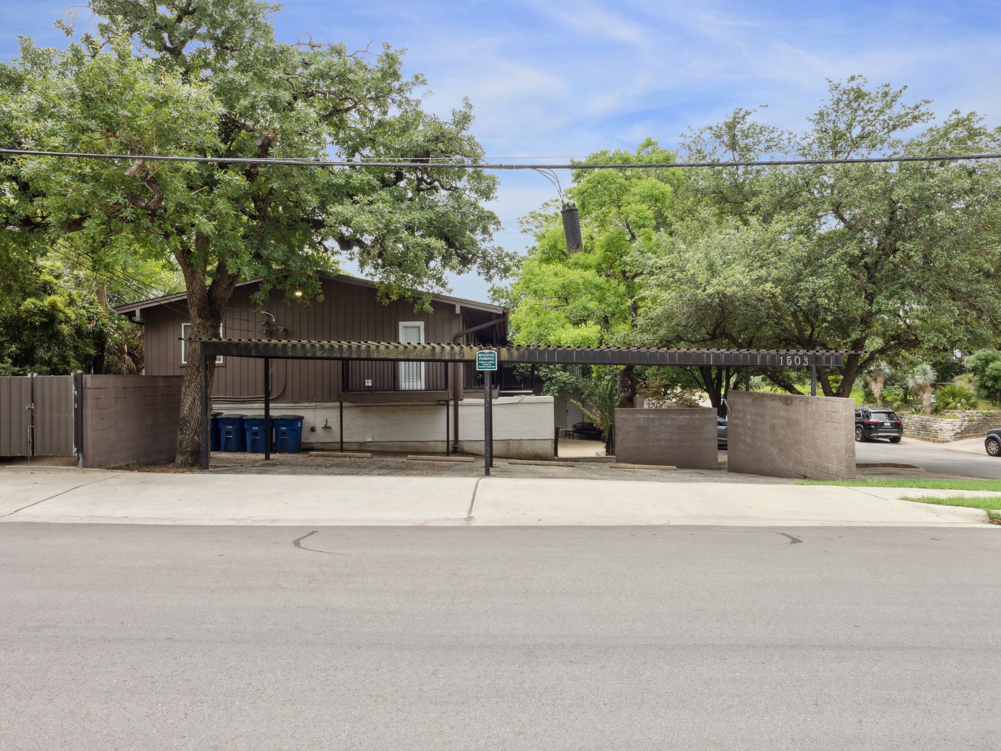 1503 West 9th Street, Unit 204 Austin, TX 78703 - Photo 20 of 21 Exterior property featuring a brown siding facade, mature trees, a multi-car carport, and a concrete driveway