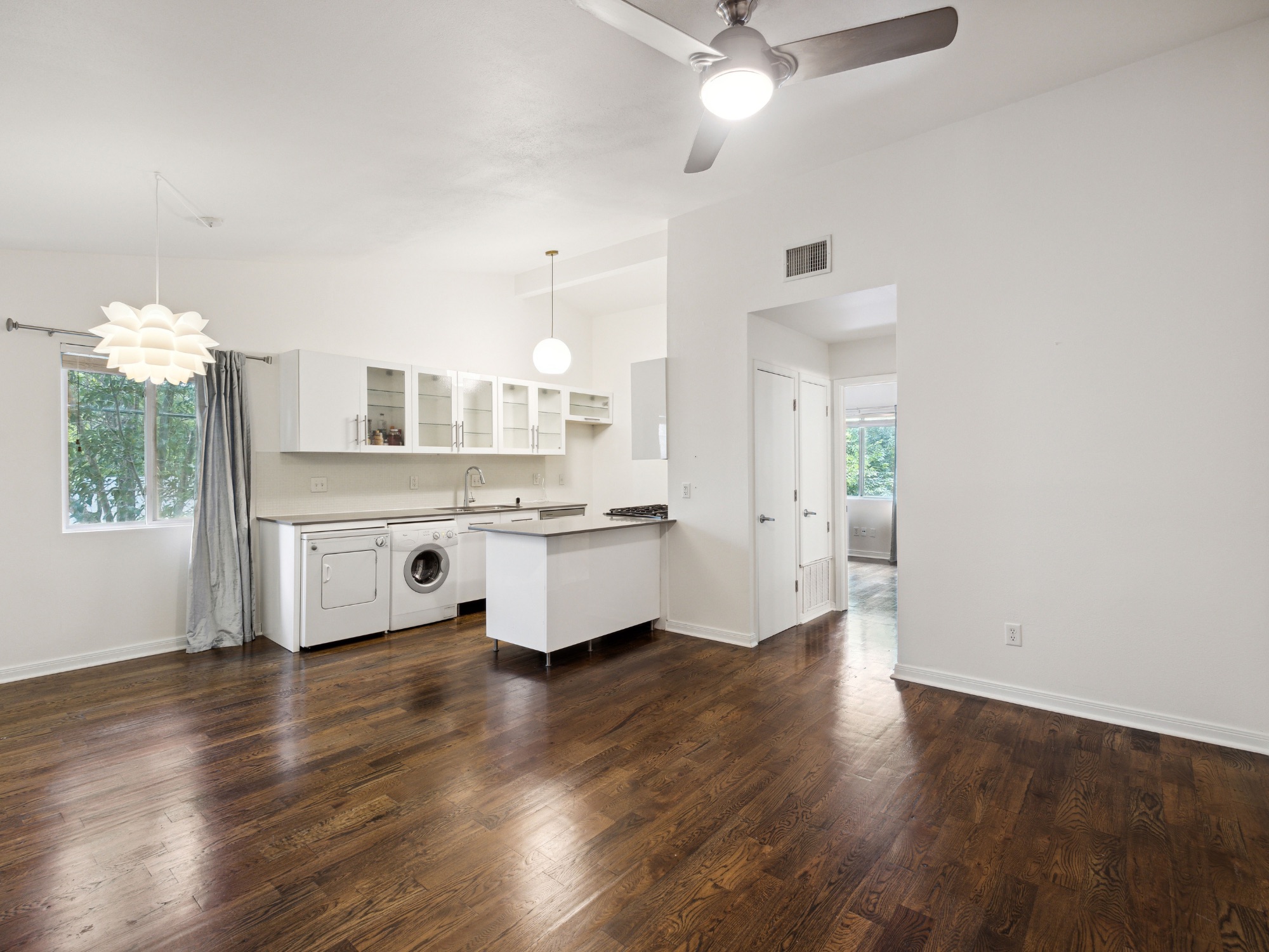 1503 West 9th Street, Unit 204 Austin, TX 78703 - Photo 7 of 21 Open-concept living area with wood-finish flooring, a kitchen featuring white cabinetry and an island, white appliances including a washing machine and dryer, and a contemporary ceiling fan with integrated lighting
