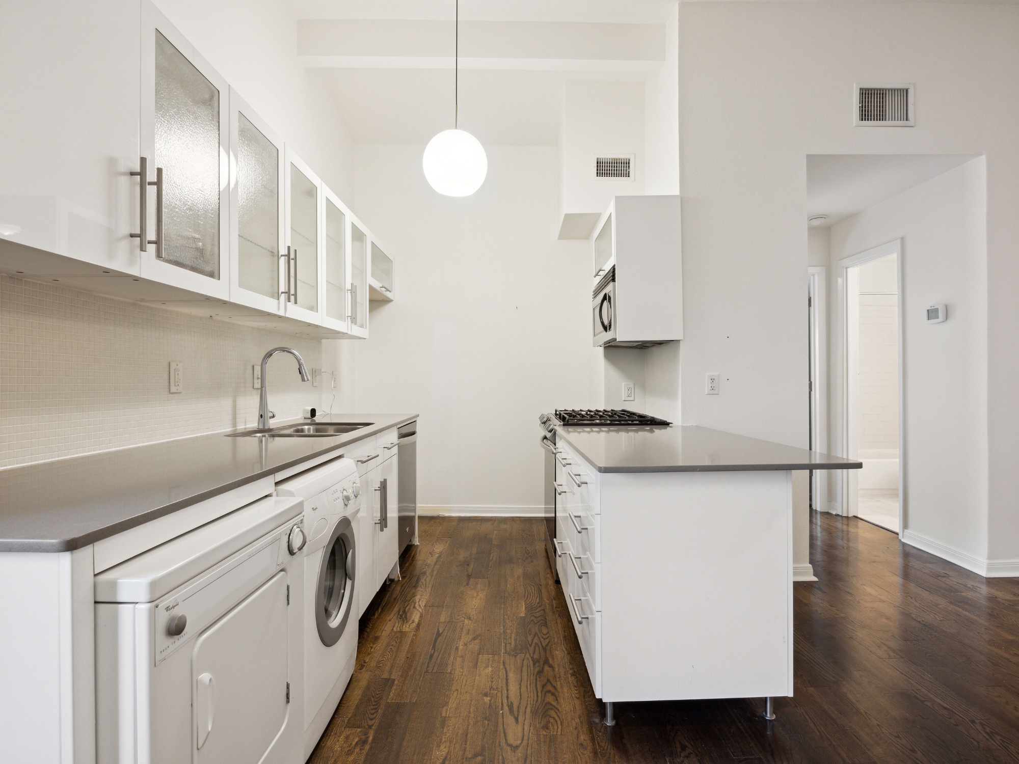1503 West 9th Street, Unit 204 Austin, TX 78703 - Photo 9 of 21 Contemporary galley kitchen featuring wood-finish flooring, white cabinetry with frosted glass inserts, a built-in microwave, a gas range, and a washer and dryer