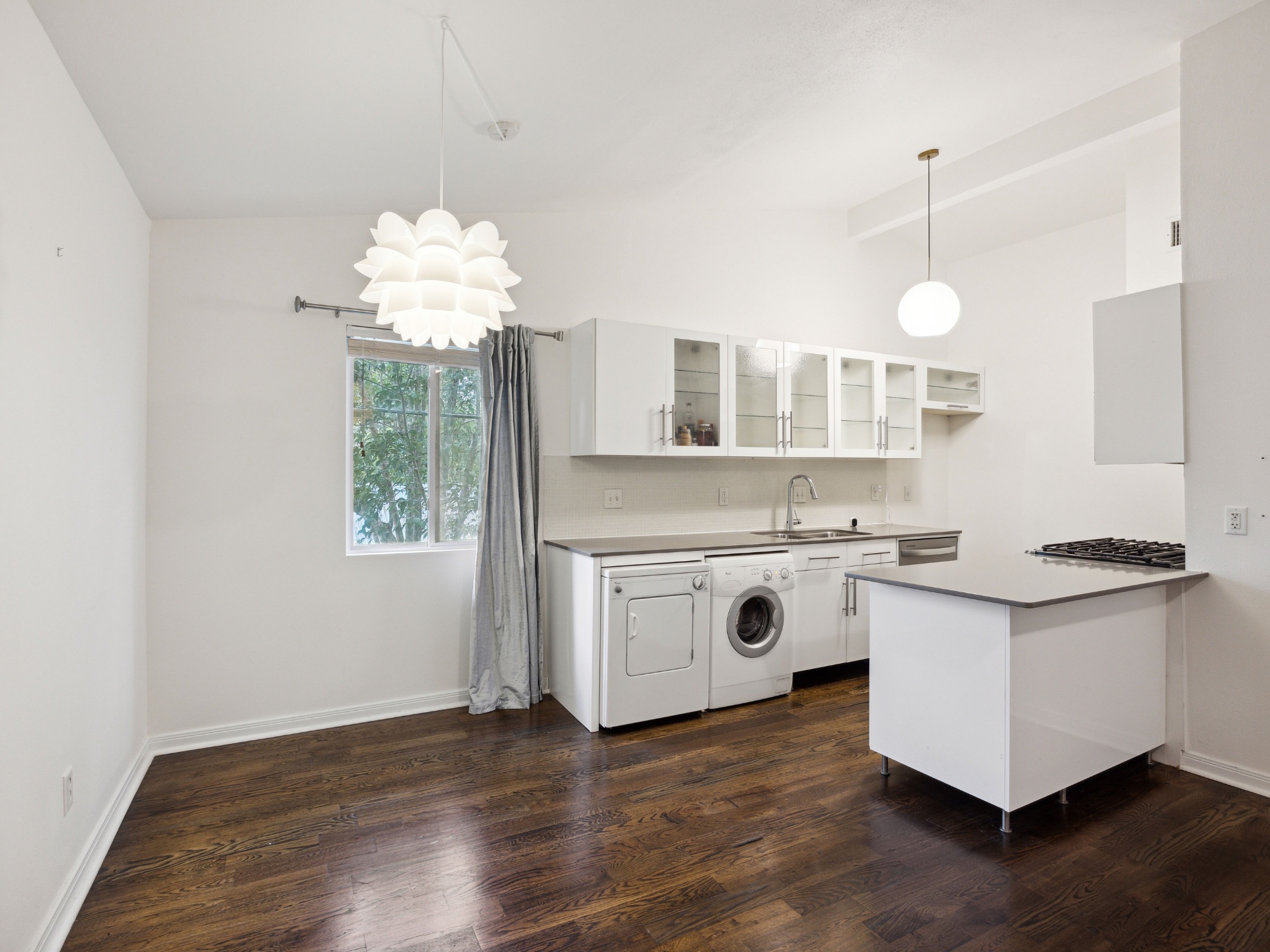 1503 West 9th Street, Unit 204 Austin, TX 78703 - Photo 10 of 21 Modern kitchen and living area featuring dark wood-finish flooring, white cabinetry with glass inserts, integrated washer and dryer units, a gas cooktop, and a kitchen island with a light-colored countertop