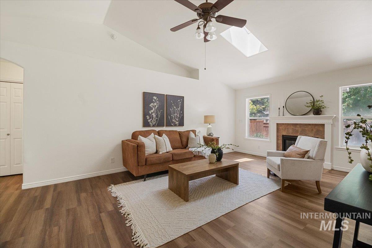 2032 Talus Loop Twin Falls, ID 83301 - Photo 12 of 43 Vaulted ceiling living room featuring wood-finish flooring, a fireplace with a white mantel and tiled surround, multiple windows, and a ceiling fan with integrated lighting