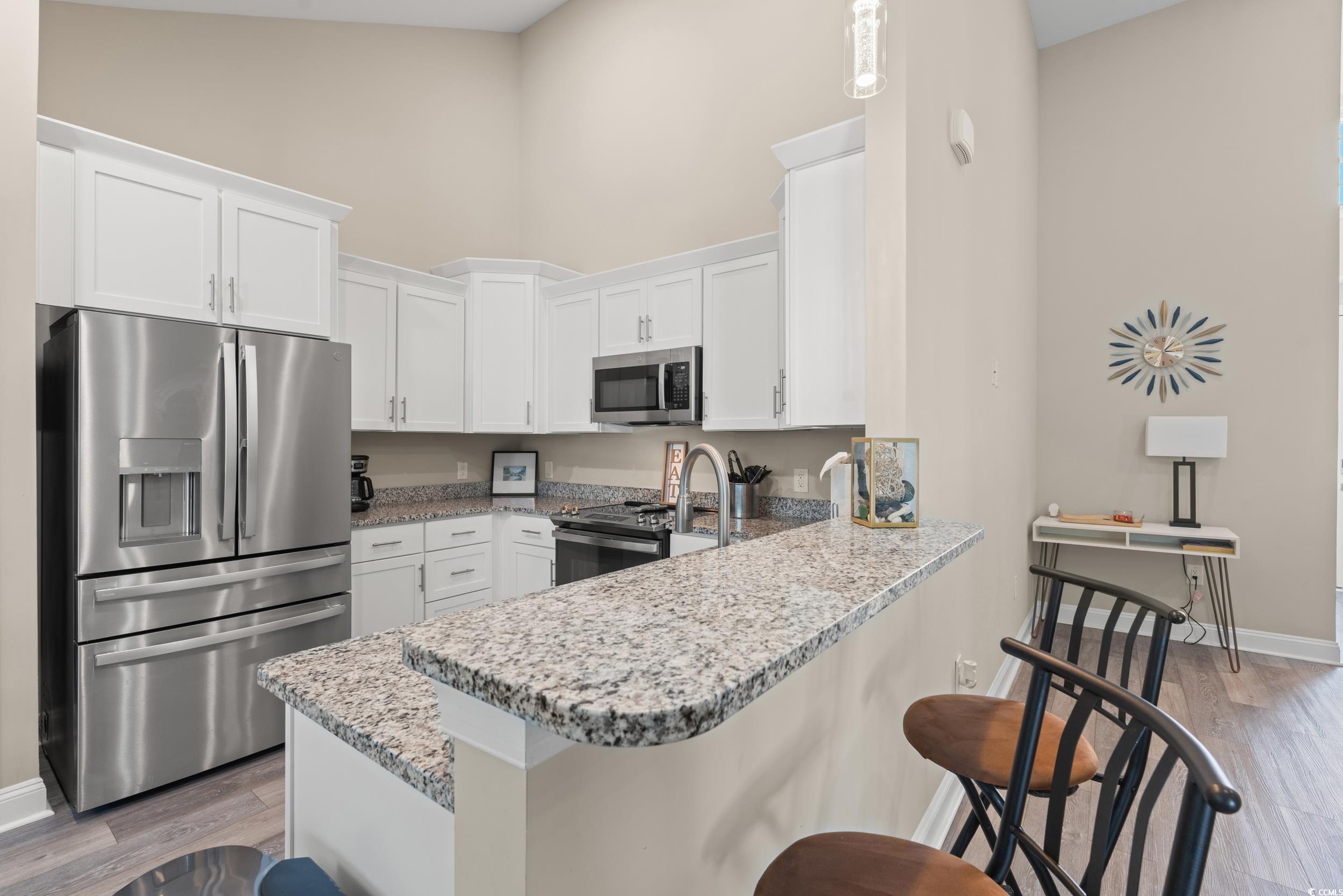 714 Charlotte Road Myrtle Beach, SC 29577 - Photo 9 of 30 Kitchen with appliances with stainless steel finishes, light wood-style floors, white cabinetry, a peninsula, and a high ceiling