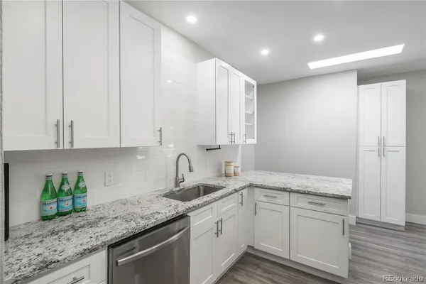 a kitchen with a sink dishwasher and white cabinets with wooden floor