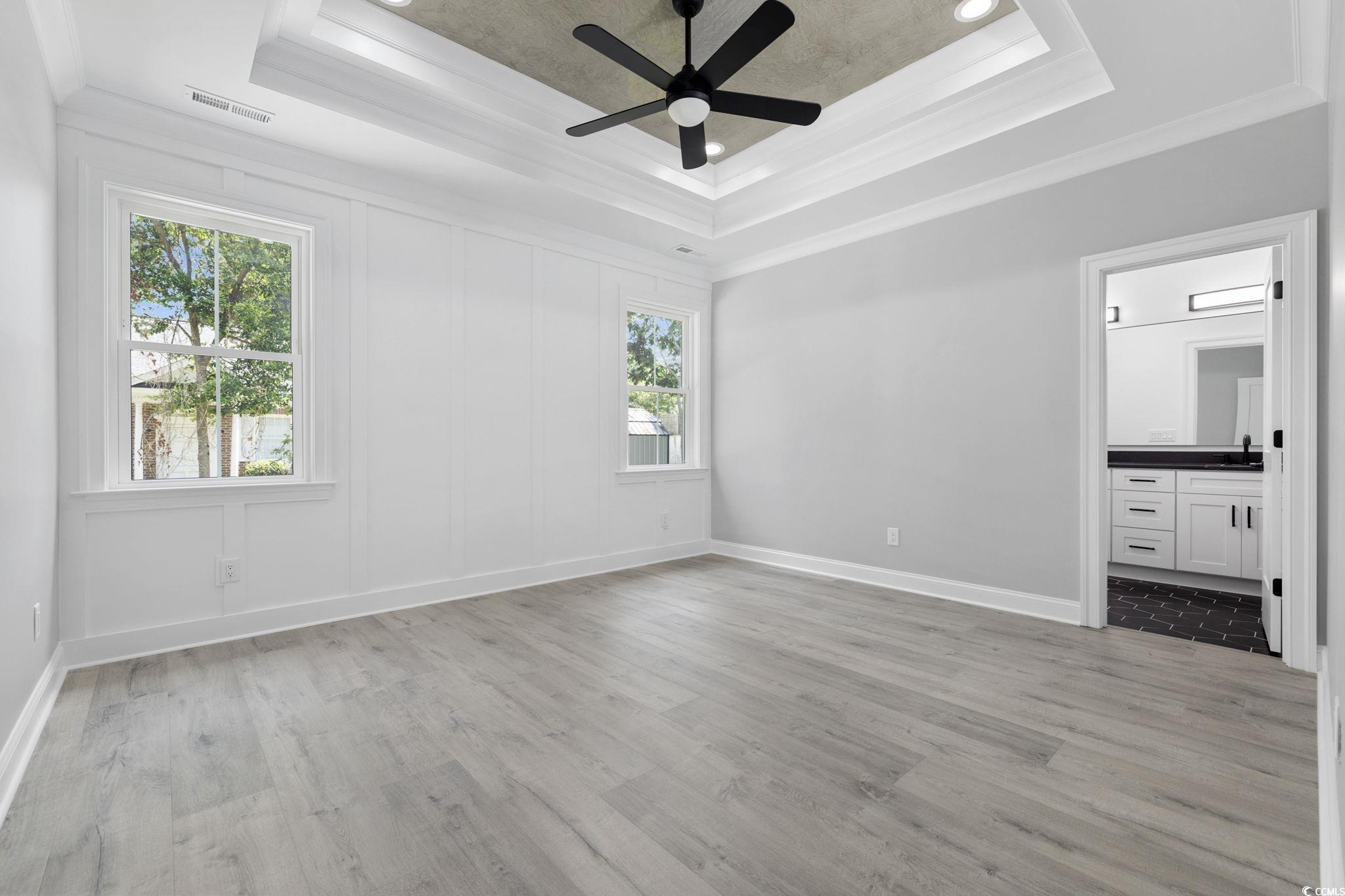 4806 North Kings Highway Myrtle Beach, SC 29577 - Photo 11 of 38 Unfurnished bedroom with crown molding, a tray ceiling, light wood-type flooring, ensuite bath, and ceiling fan