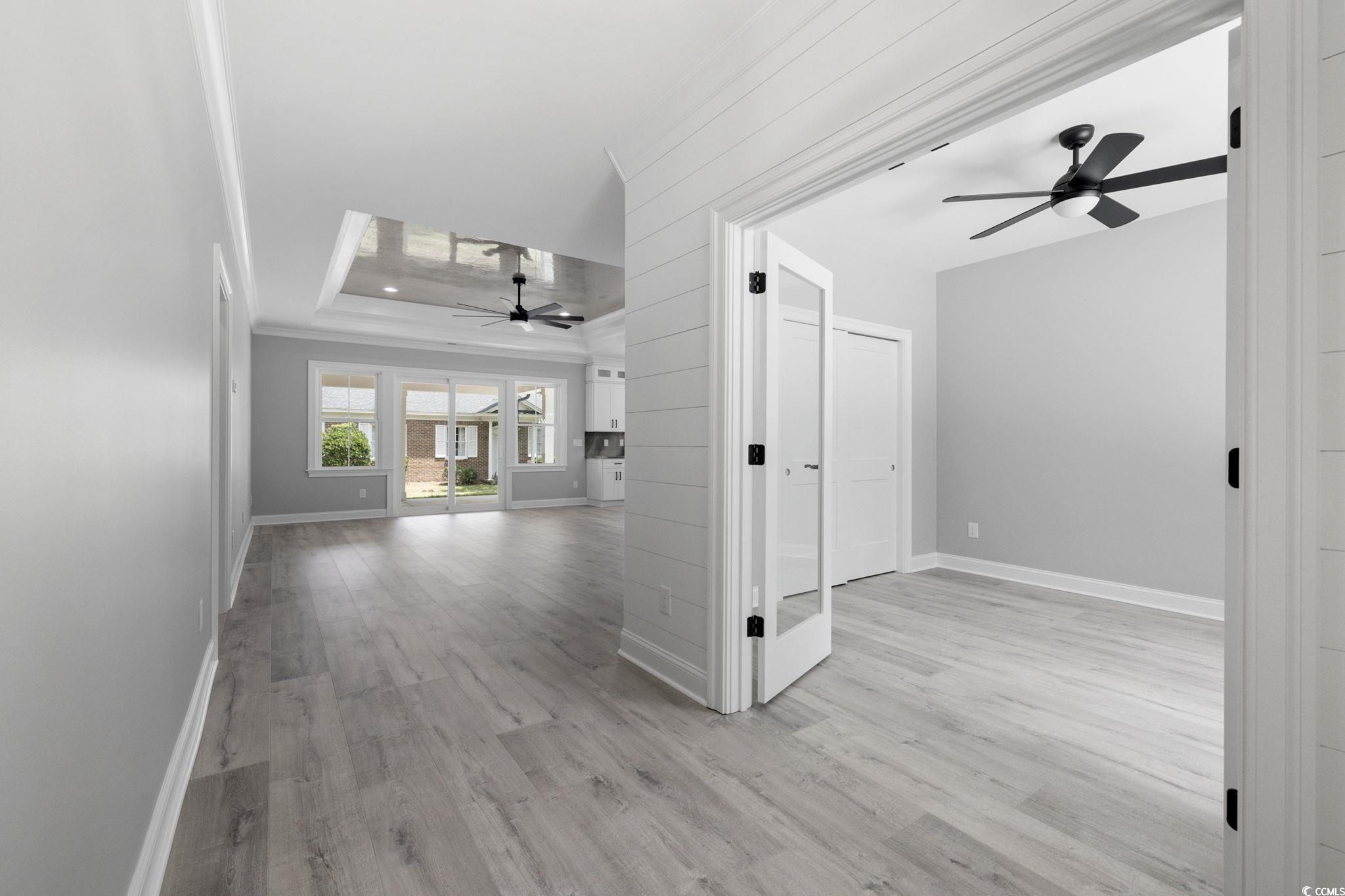 4806 North Kings Highway Myrtle Beach, SC 29577 - Photo 30 of 38 Unfurnished living room with ceiling fan, a raised ceiling, light wood-style floors, and crown molding