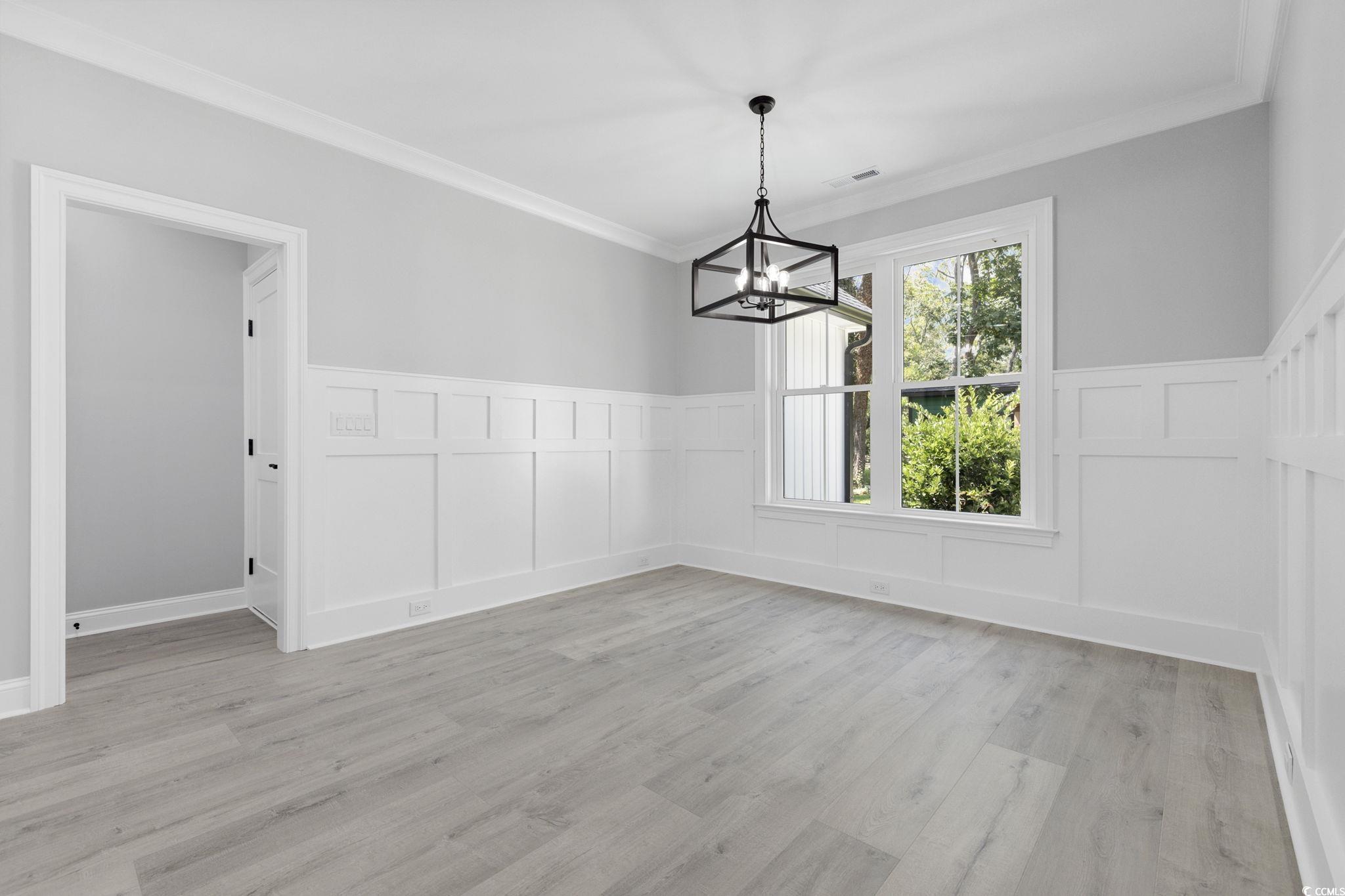 4806 North Kings Highway Myrtle Beach, SC 29577 - Photo 9 of 38 Unfurnished dining area with a decorative wall, a wainscoted wall, a chandelier, ornamental molding, and light wood-style flooring