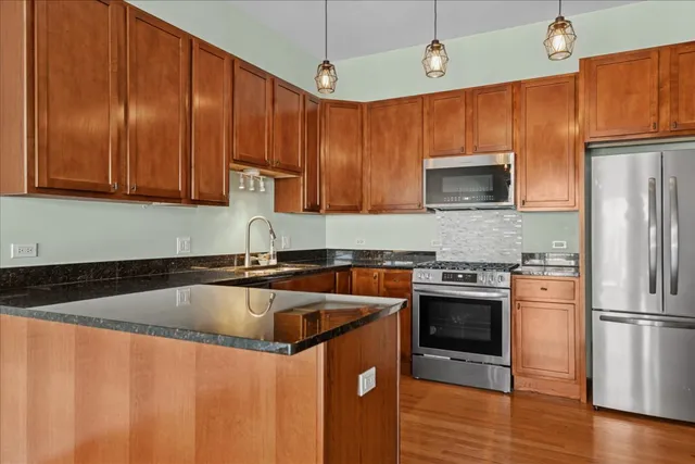 a kitchen with stainless steel appliances granite countertop a sink a stove a refrigerator cabinets and wooden floor